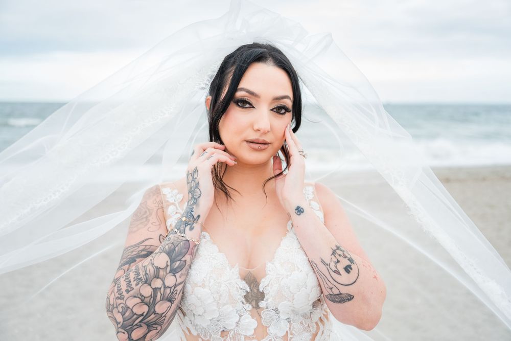 Artistic bridal portrait with flowing veil against ocean backdrop.