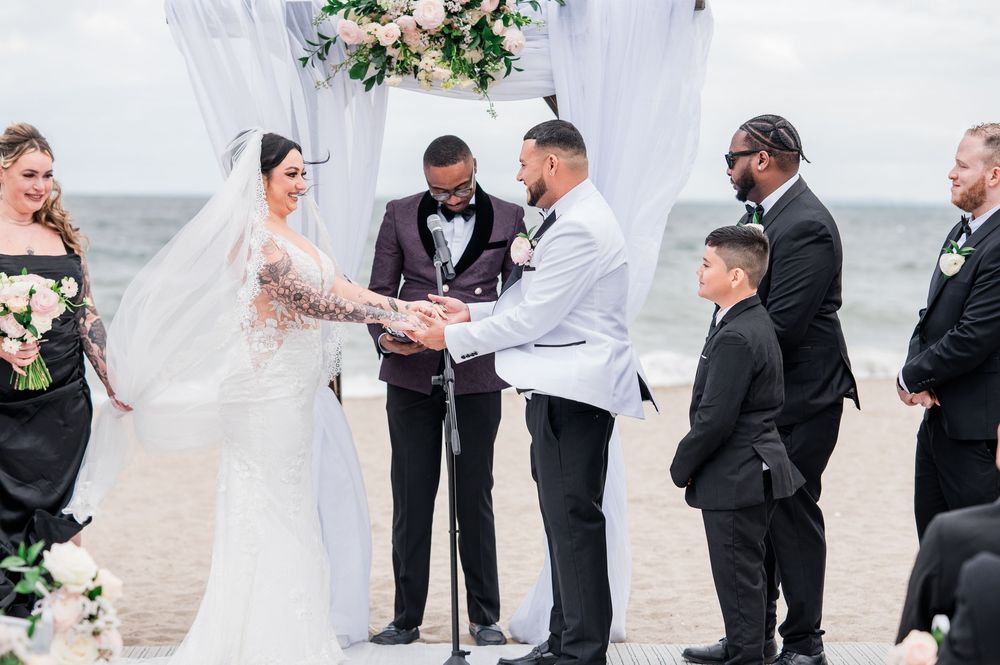 Beach wedding ceremony with white draping and floral arrangements.