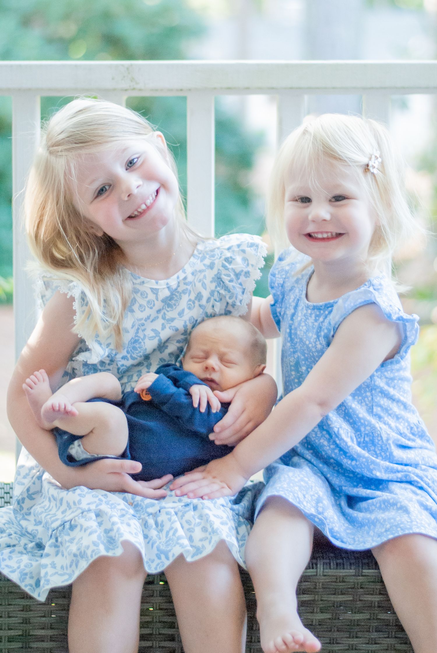 2 sisters embracing their sweet newborn baby brother during an in home family session