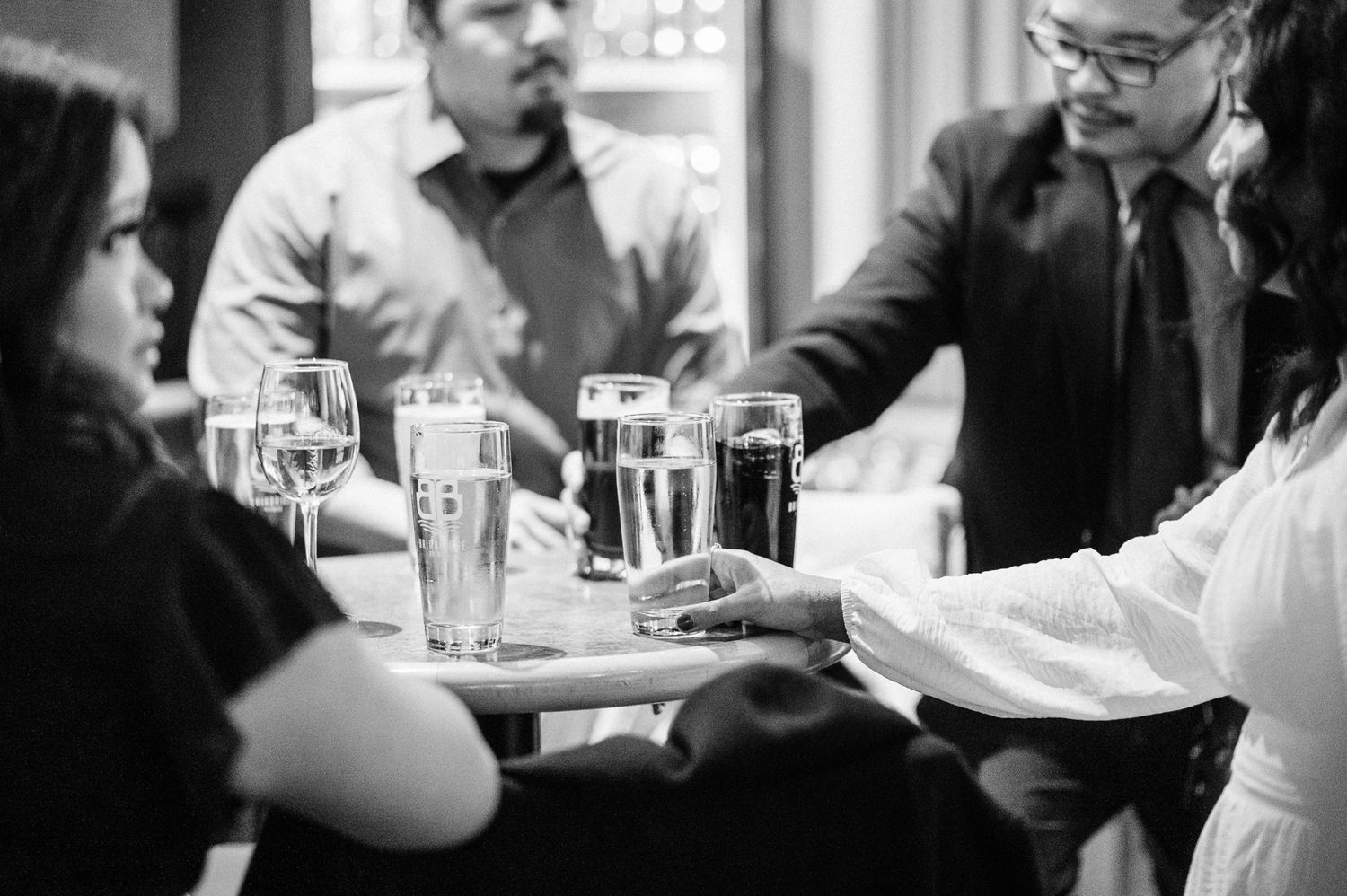 A black and white photo showing hands and drinks at a brewery  during a wedding recpetion