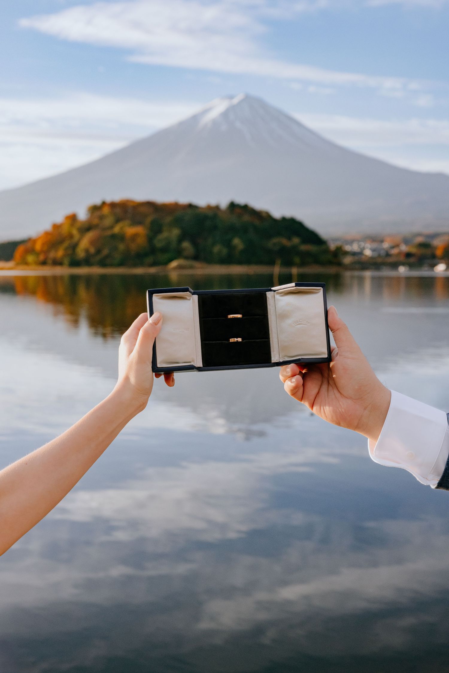 Hands hold a ring box against the backdrop of Mount Fuji and Lake Kawaguchiko in Japan during autumn.