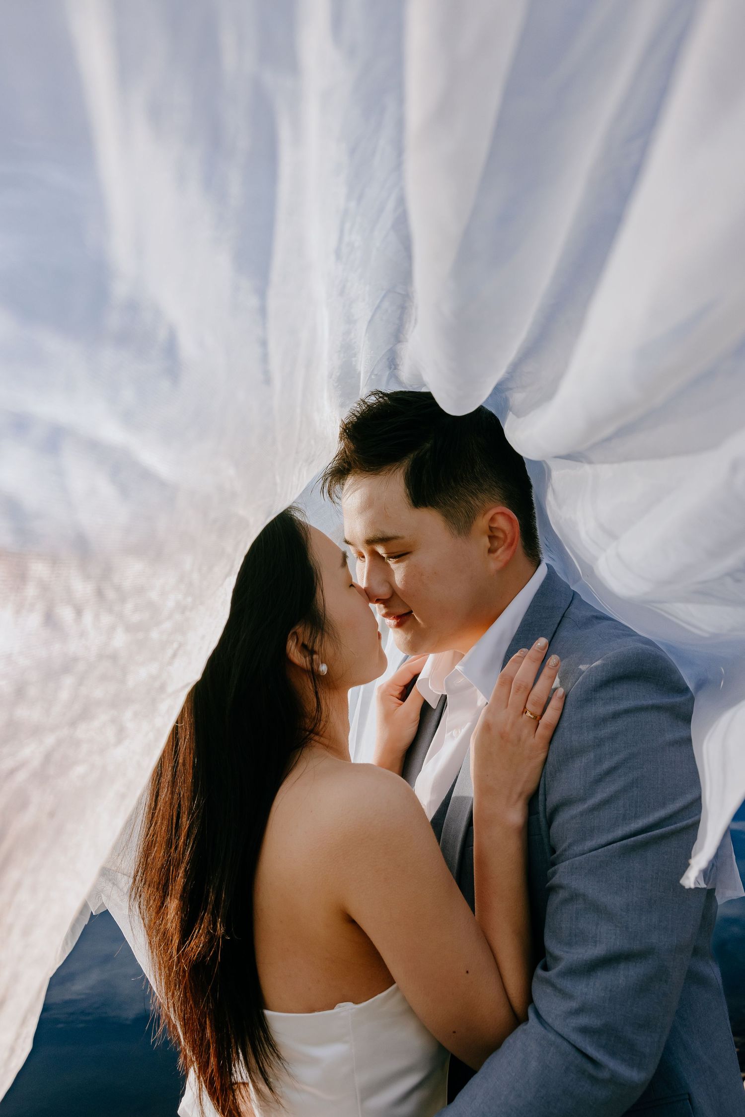 A romantic couple in wedding attire share an intimate kiss against flowing white fabric backdrop in a photo series.
