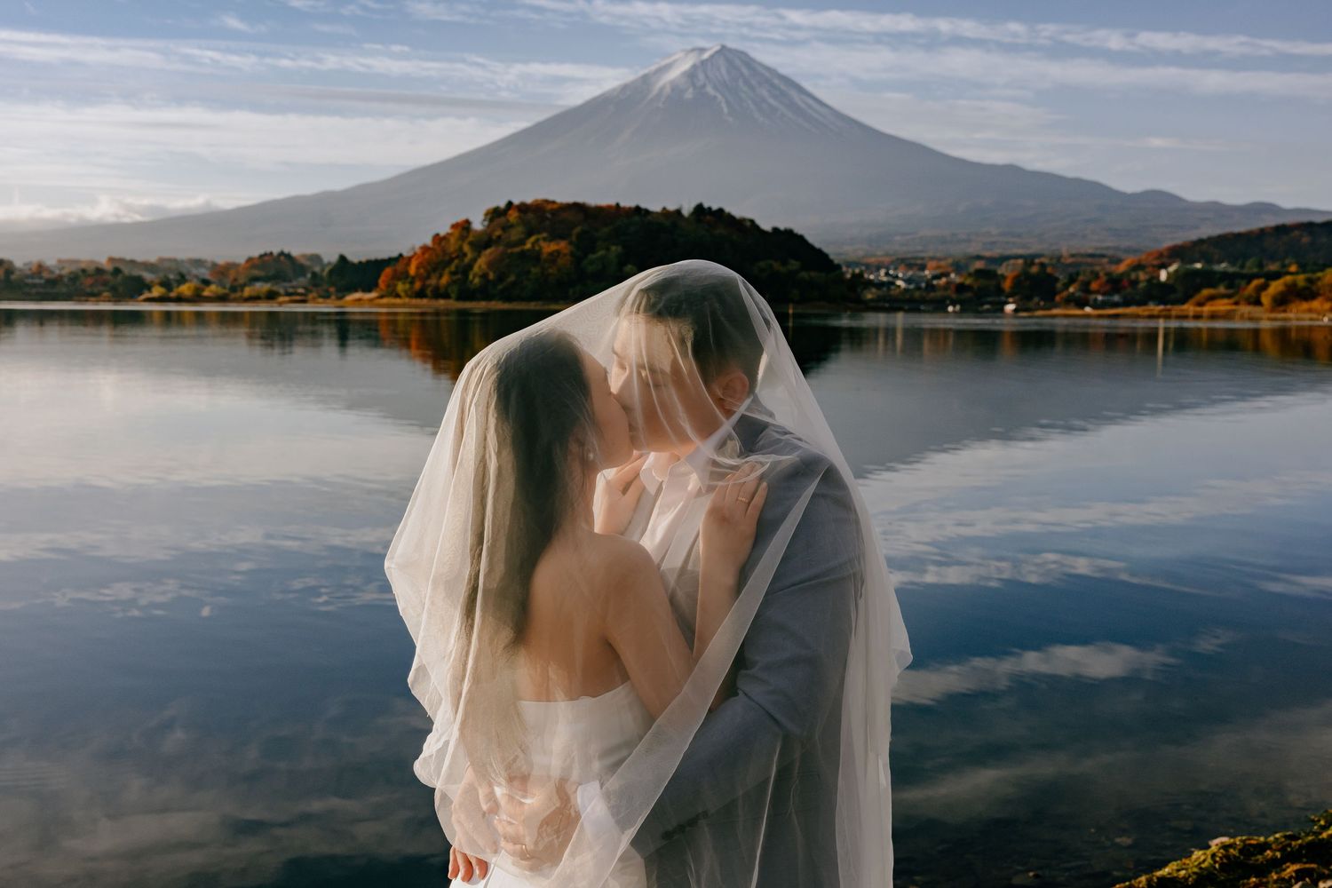 Mount Fuji towers majestically over a serene lake with reflections of clouds in the calm waters at sunset.