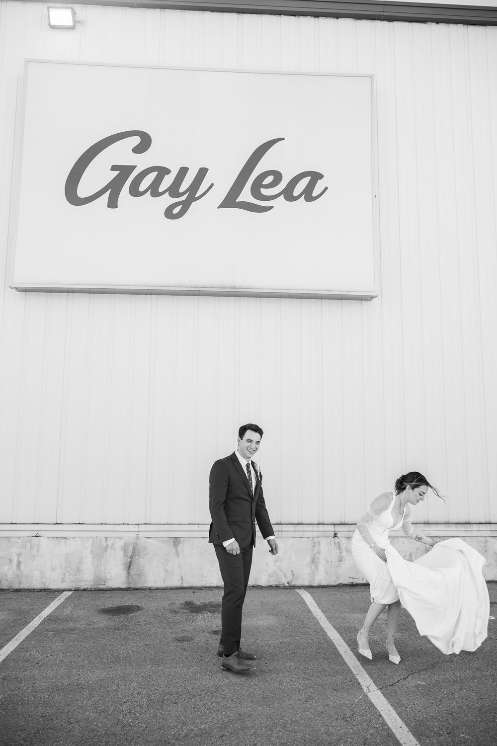 A minimalist black and white photo series showing a couple in formal attire creating playful poses against a plain wall.