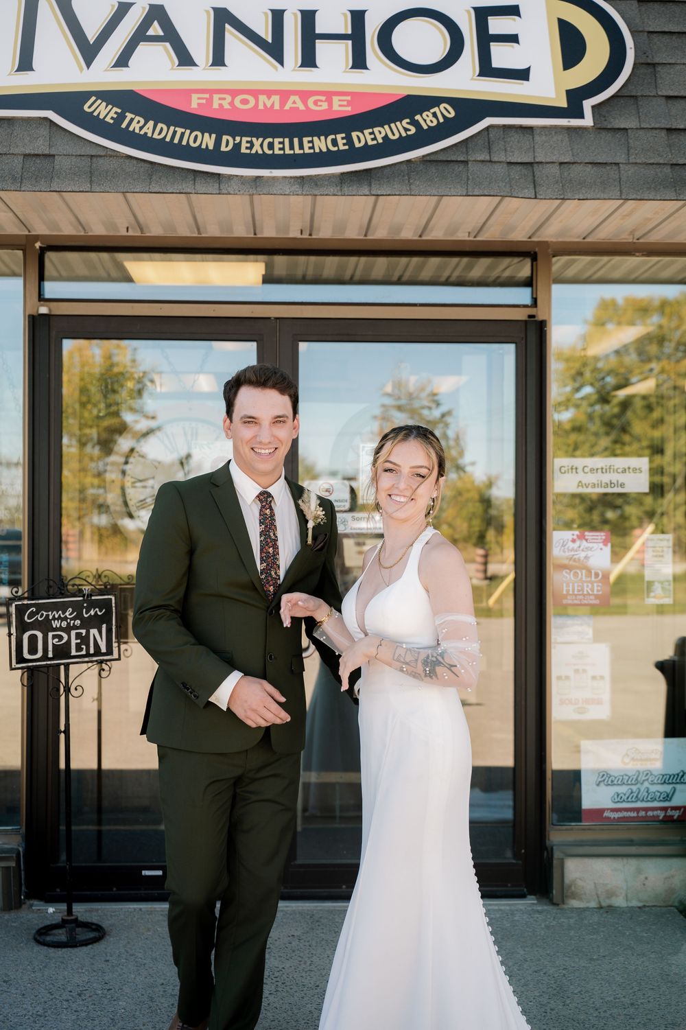A couple poses in formal attire outside a storefront with a large 'Ivanhoe' sign above.