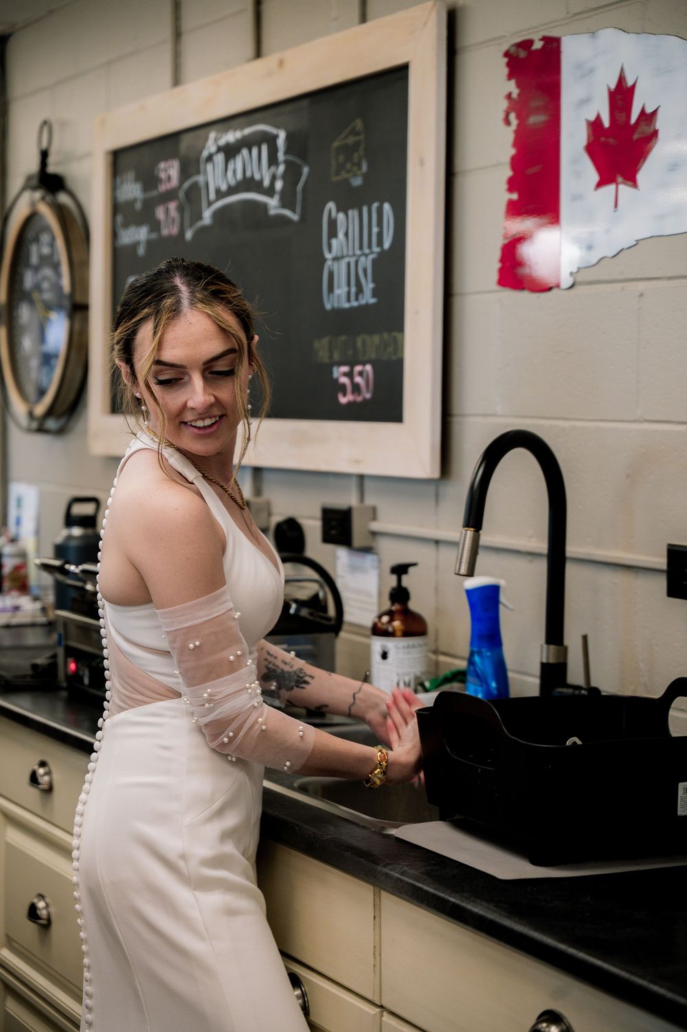 Woman in white dress stands in modern kitchen with Canadian maple leaf artwork displayed on wall behind her.