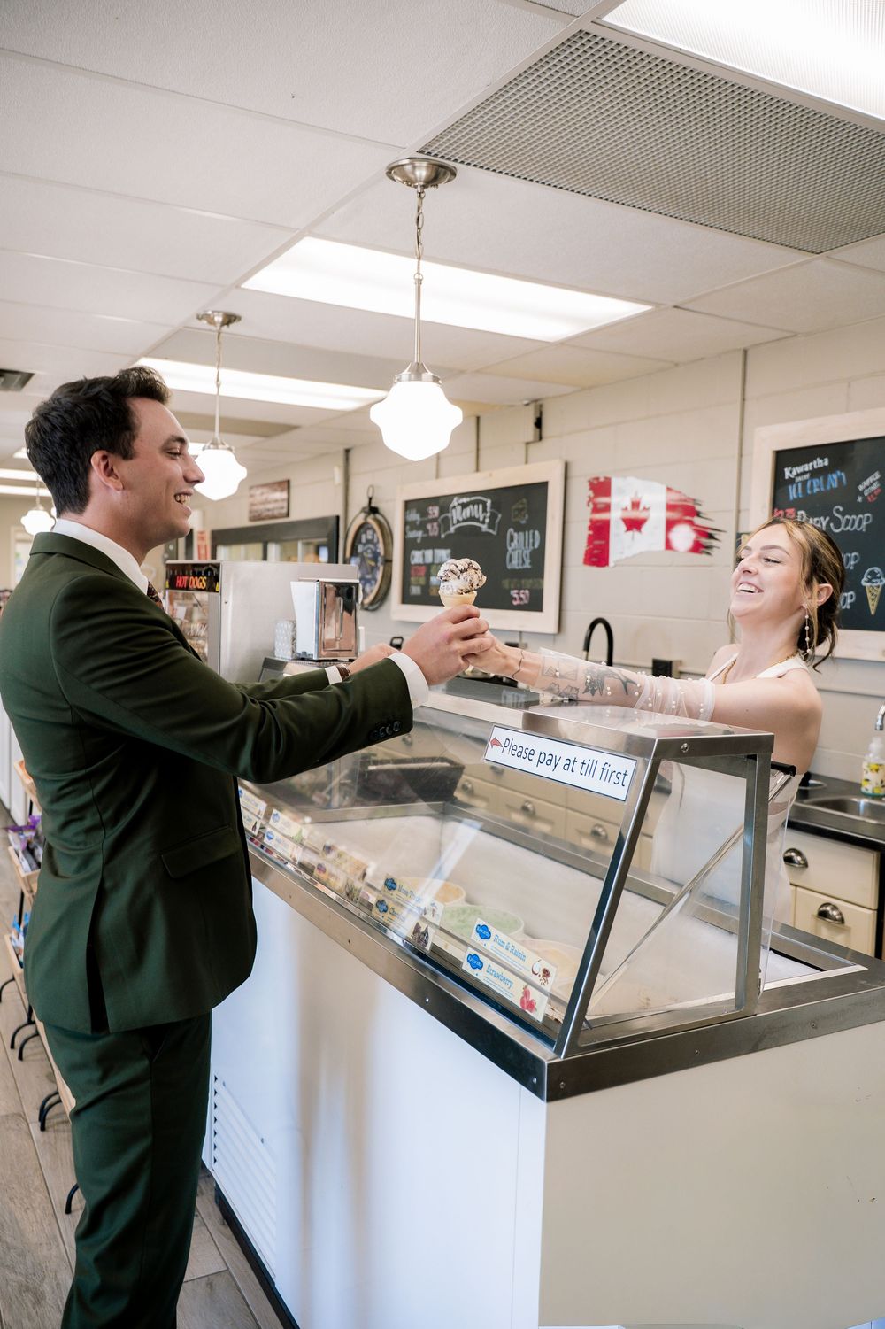 Customer being served at an ice cream shop counter with a display case and pendant lights overhead.