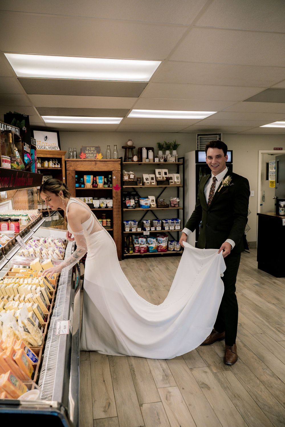Couple in formal attire playfully holding white fabric across a store aisle with light wood flooring.