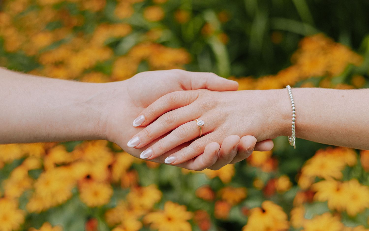 Close-up of hands reaching towards each other against a background of orange flowers.