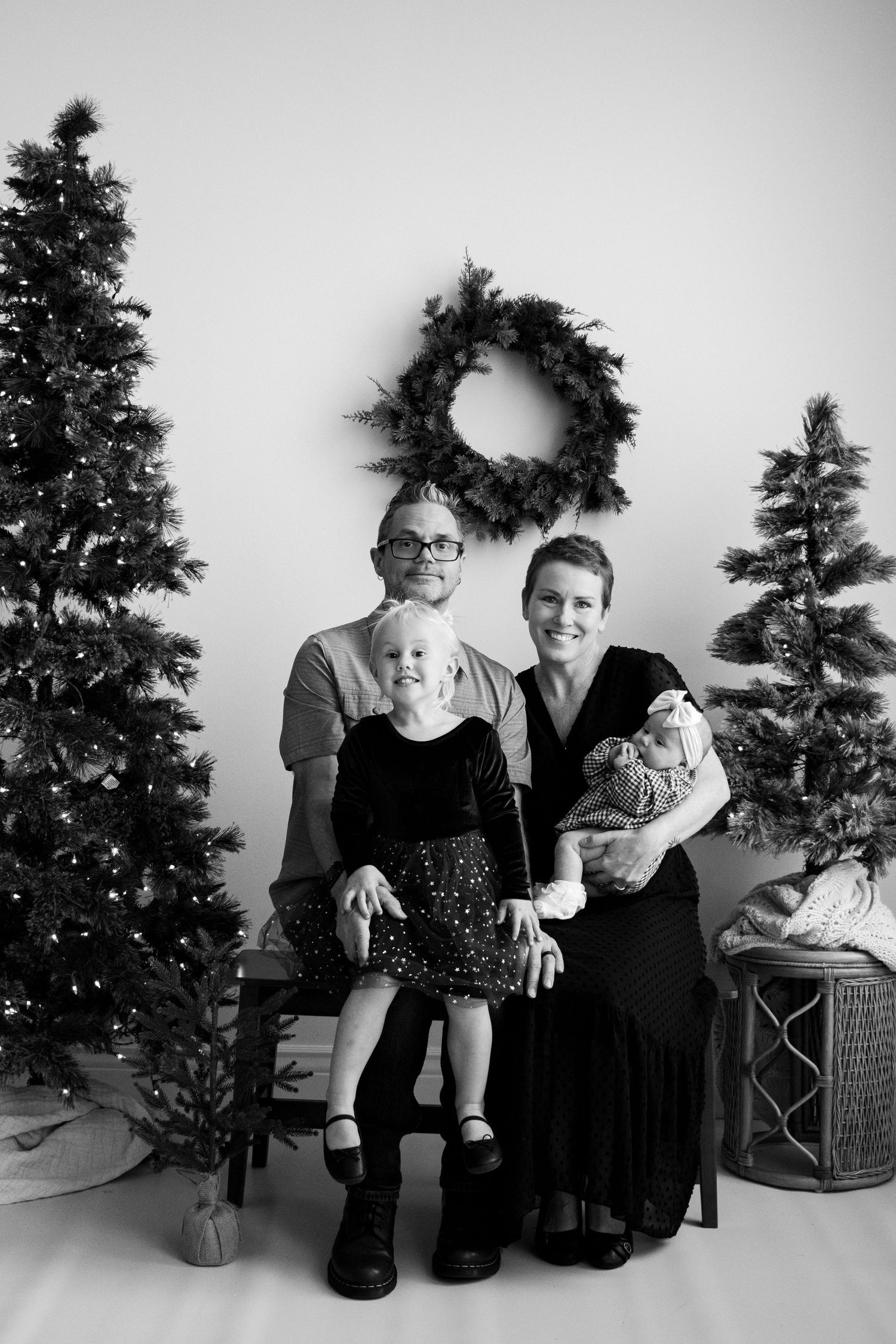 Family of four cuddled on a benchbeside a decorated Christmas tree in Roy Utah