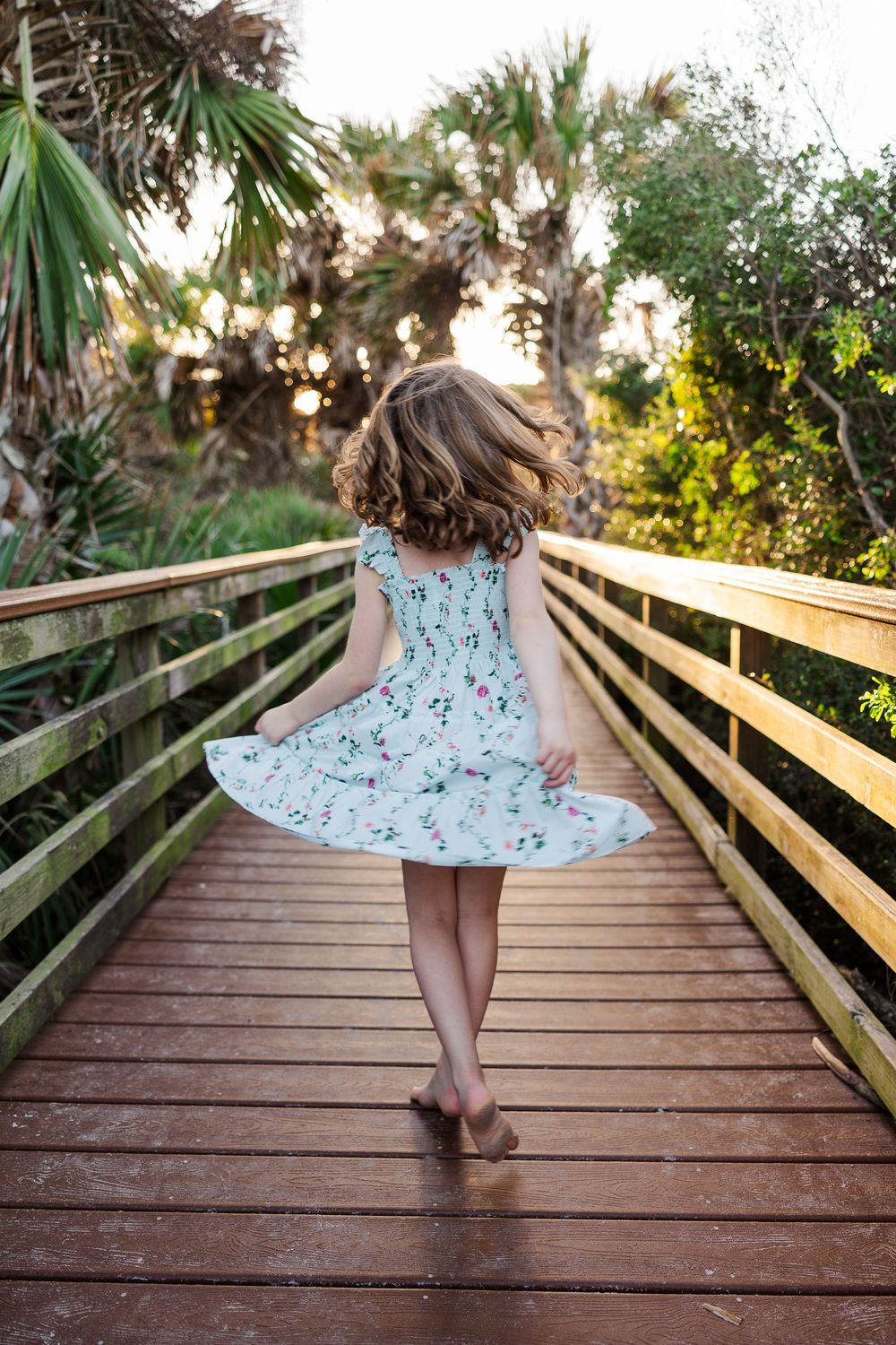 A series of photos showing a twirling dress on a wooden boardwalk surrounded by tropical foliage at sunset.