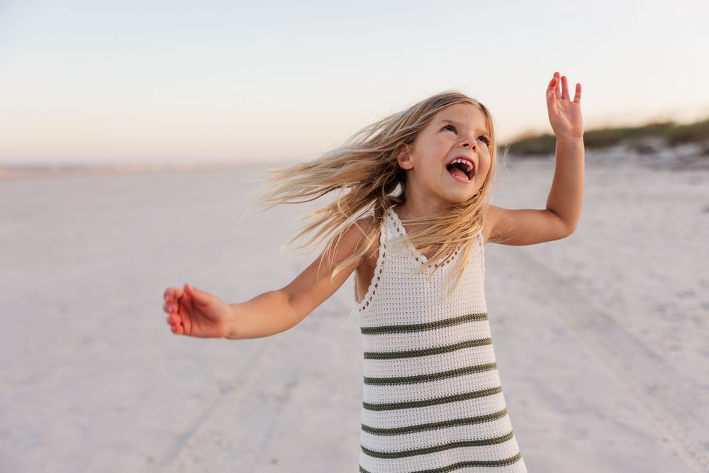 A sequence of images showing someone in a striped dress twirling and dancing joyfully on a sandy beach.