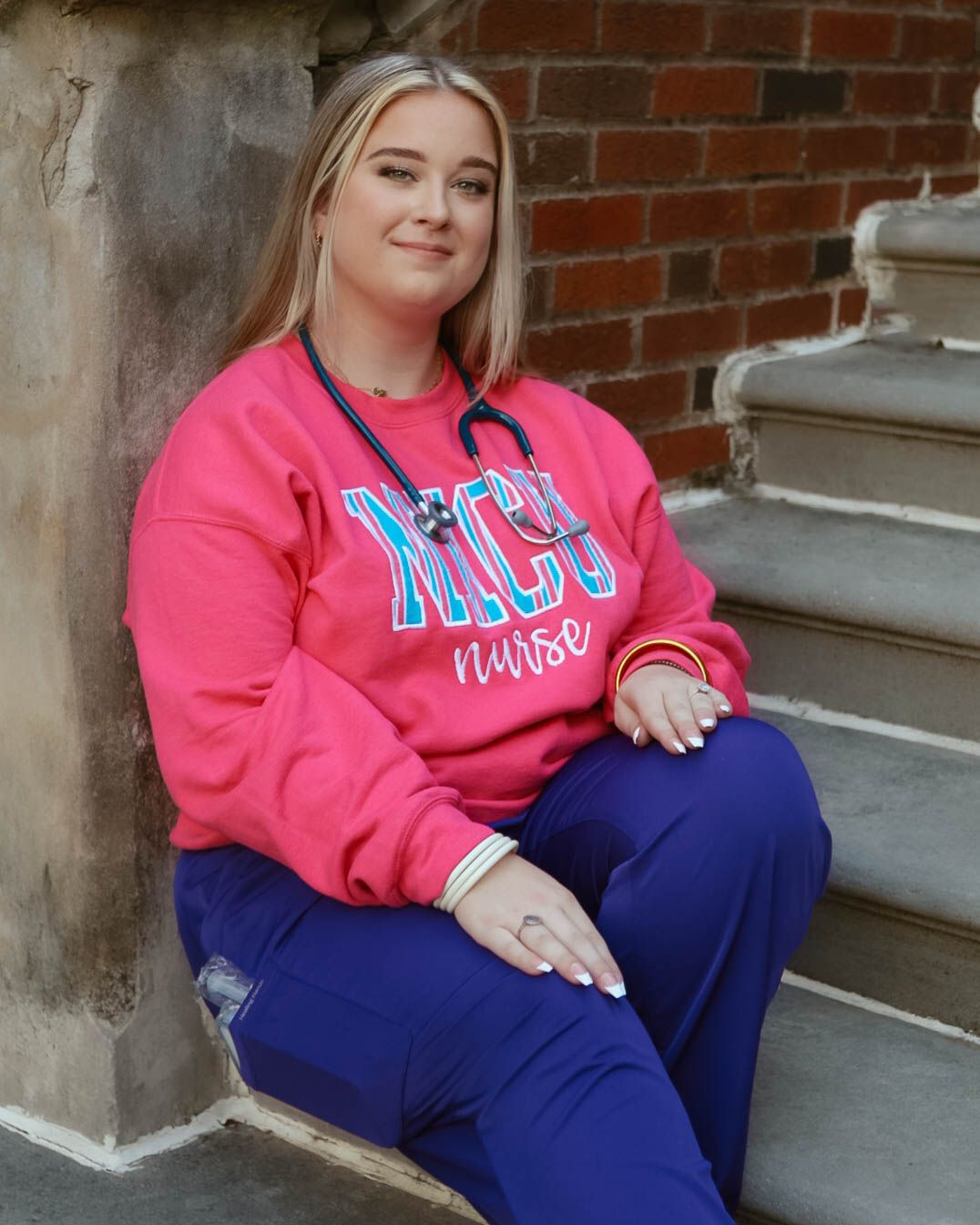 Relaxed poses on stone steps wearing bright pink sweatshirt and navy pants.