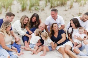 Large family group relaxing together on sandy beach with dunes in background.