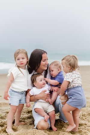 Small group of children gather around adult on sandy beach near ocean.