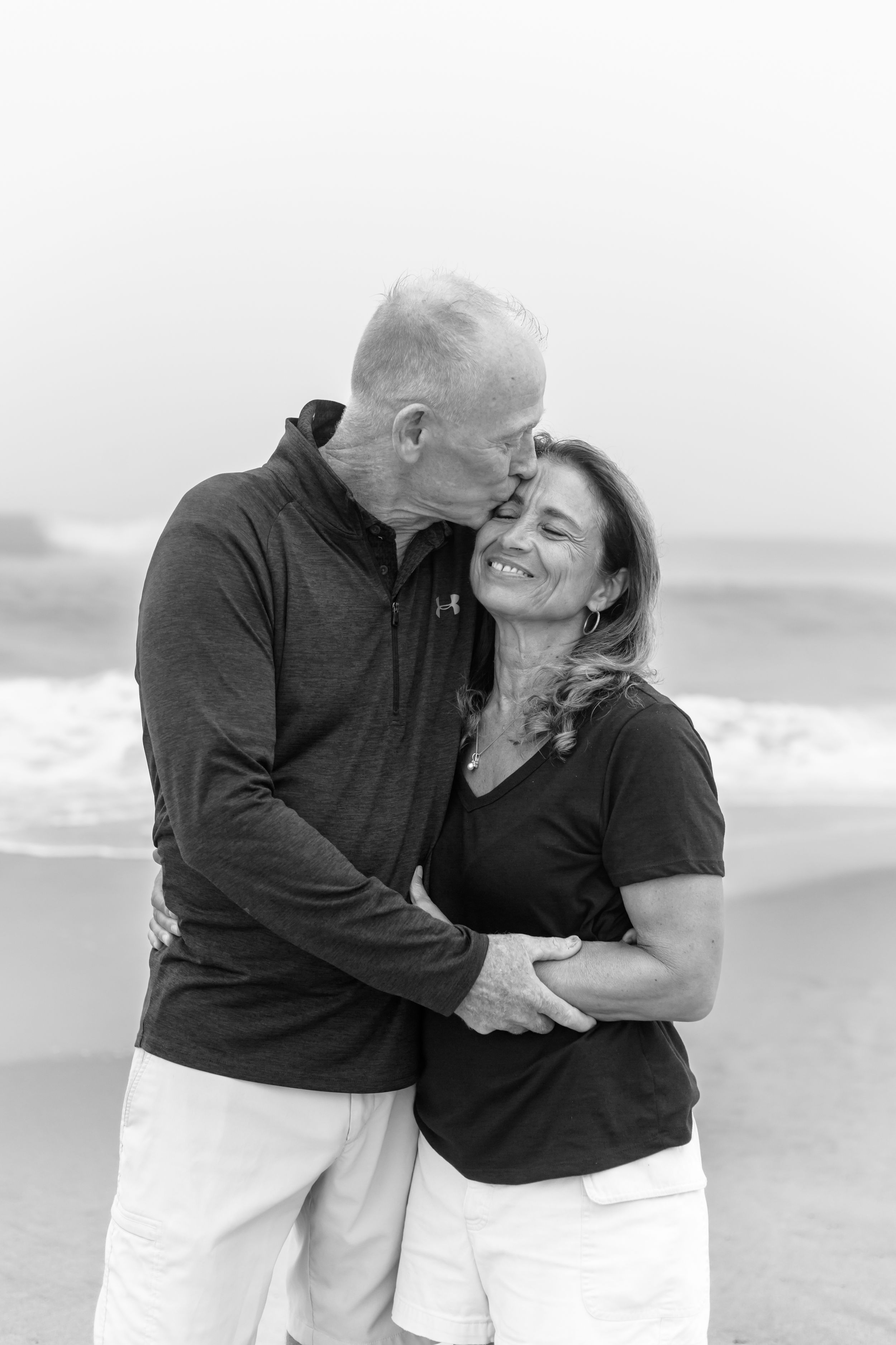 Loving couple in black sweaters sharing romantic moments on a cloudy beach.