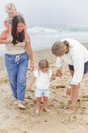 Family members bend down to examine something interesting in the sand at the beach.