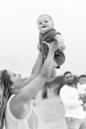 Black and white photos showing tender moments of a parent lifting a baby up in the air on a beach.