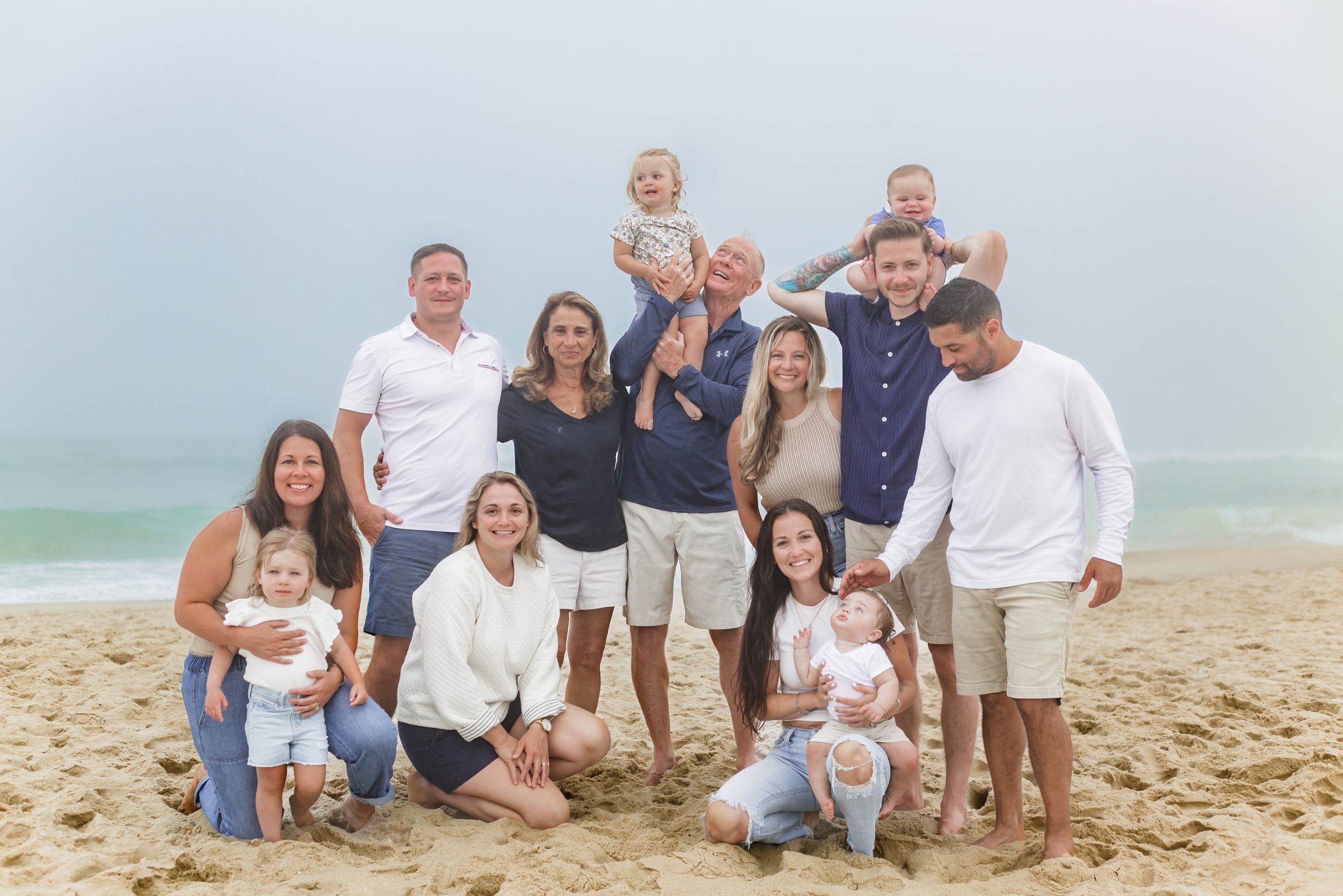 Extended family group poses together on a sunny beach with ocean waves in the background.