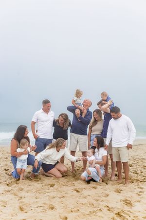Casual family gathering on sandy beach during overcast day by the ocean.