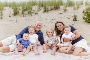 Family members lounging together on sandy beach with grass dunes in background wearing coordinated outfits.