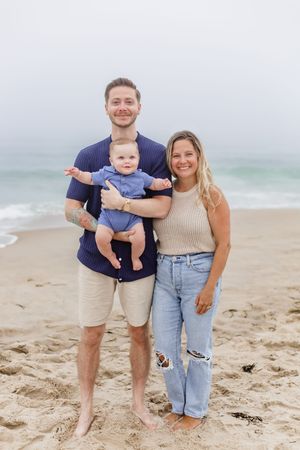A family poses together on a sunny beach with waves in the background.