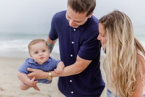Family wearing blue and white outfits shares affectionate moments together on a sunny beach.