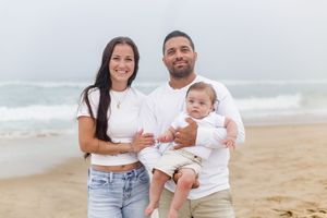 A joyful family enjoying a sunny day together at the beach with waves crashing in the background.