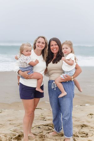 Two adults holding toddlers pose together on a cloudy beach.