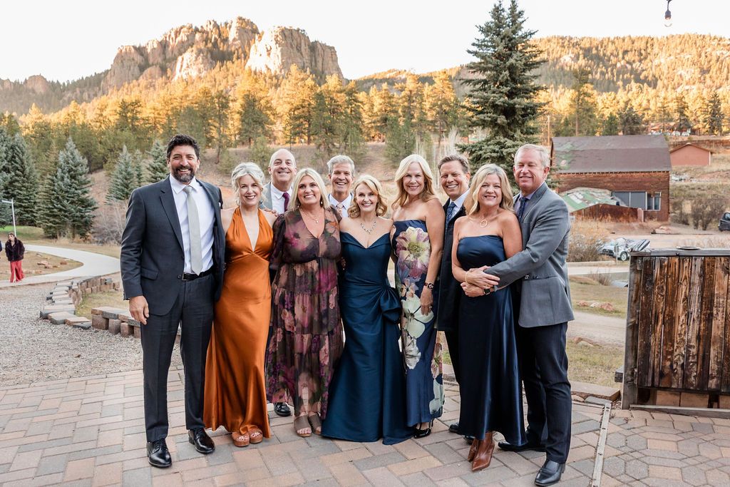 Wedding party poses together outdoors with autumn mountain scenery and evergreen trees in the background.