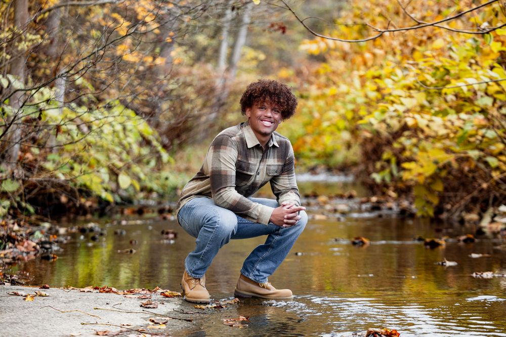 Person sitting by a stream in autumn with golden foliage reflecting in the water.