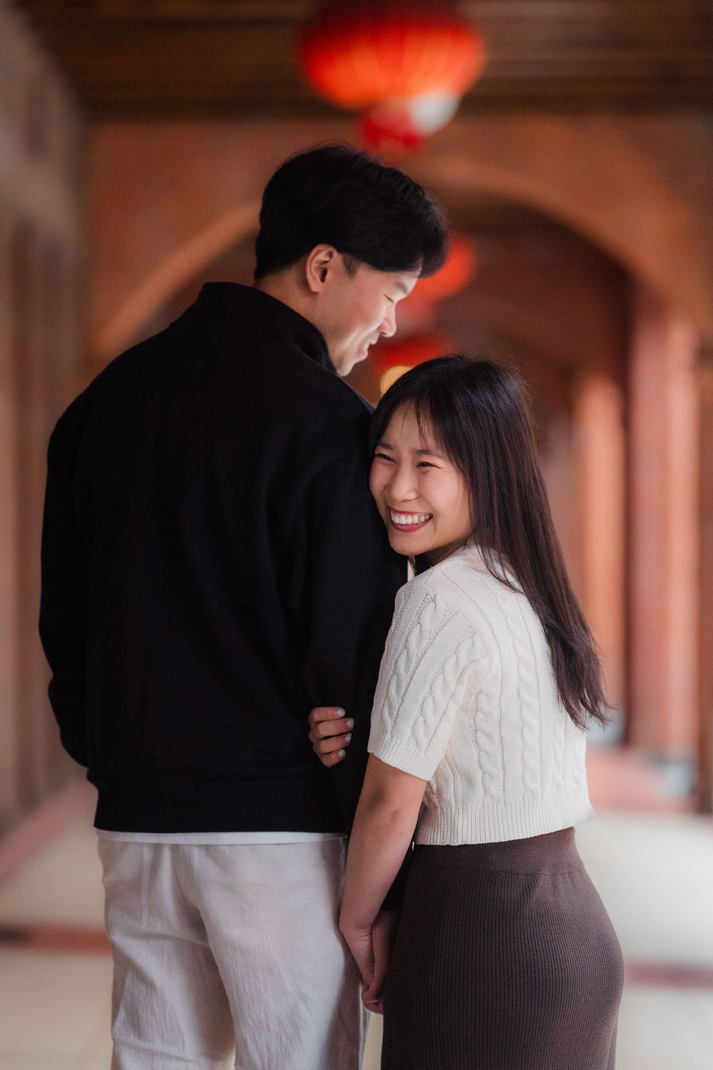 A romantic couple shares a tender moment in an arched hallway with traditional Chinese red lantern decor.