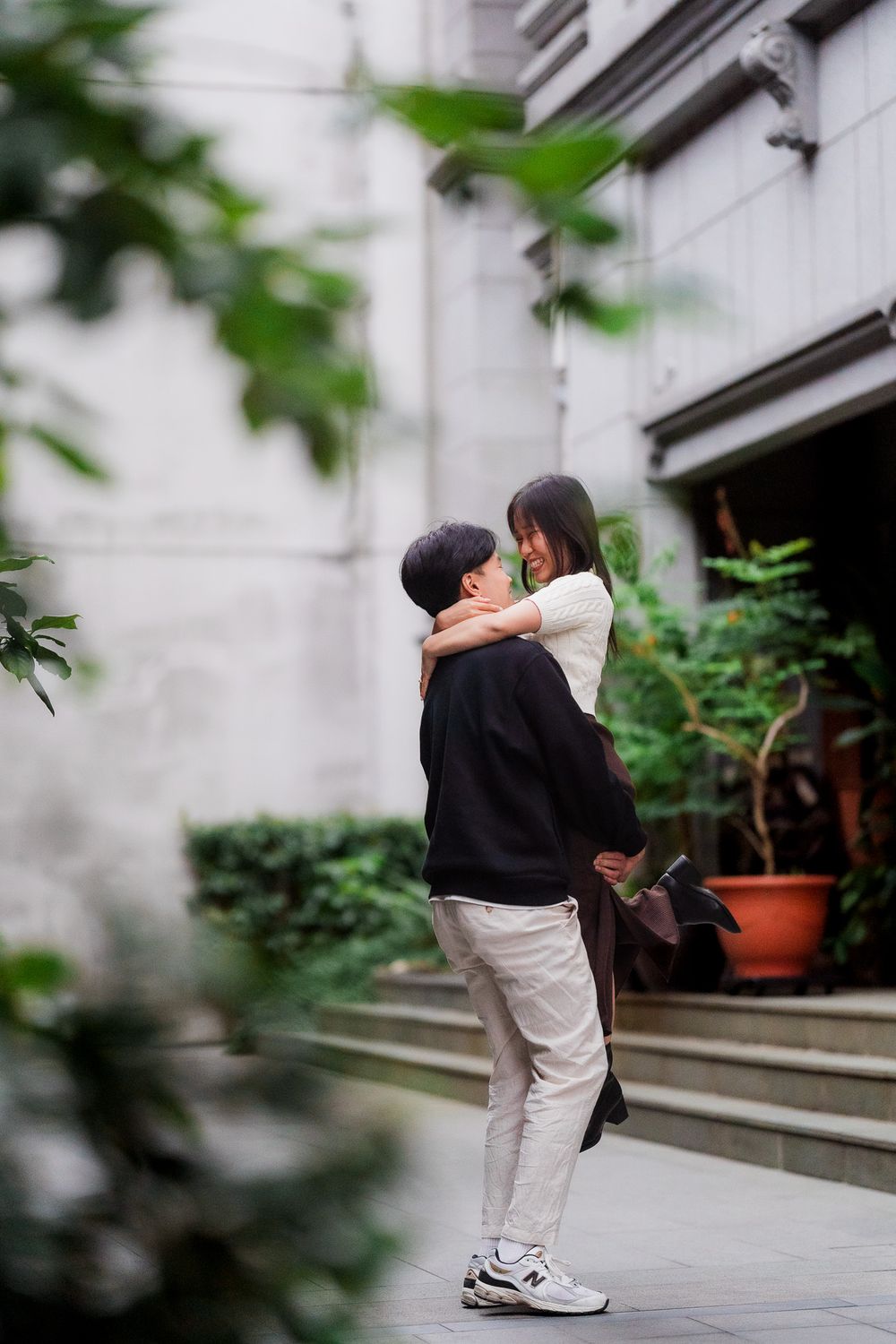 Two people in casual attire share an intimate moment while sitting on concrete steps near potted plants.