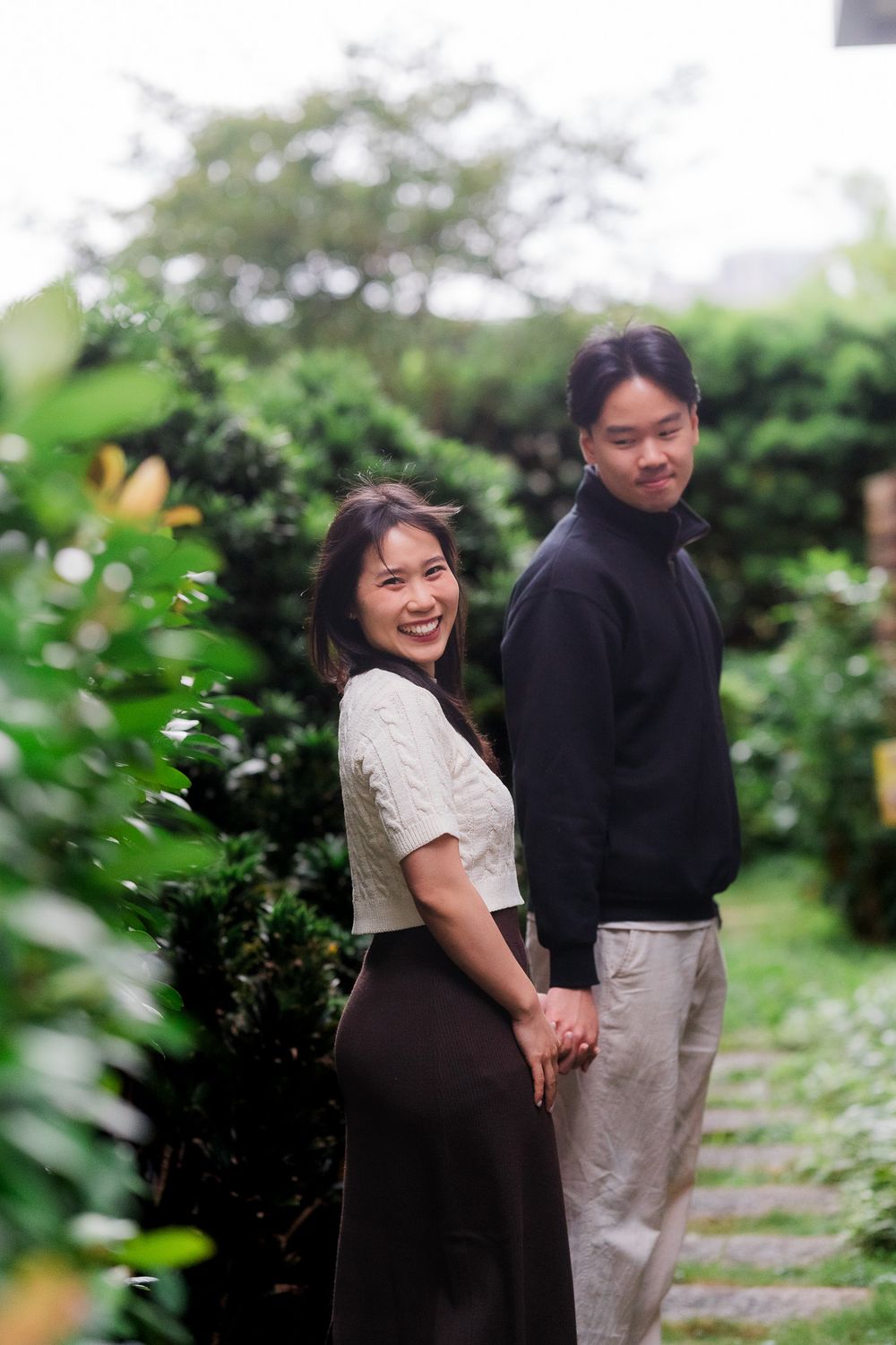 A couple shares a joyful moment together while posing in a lush garden setting.