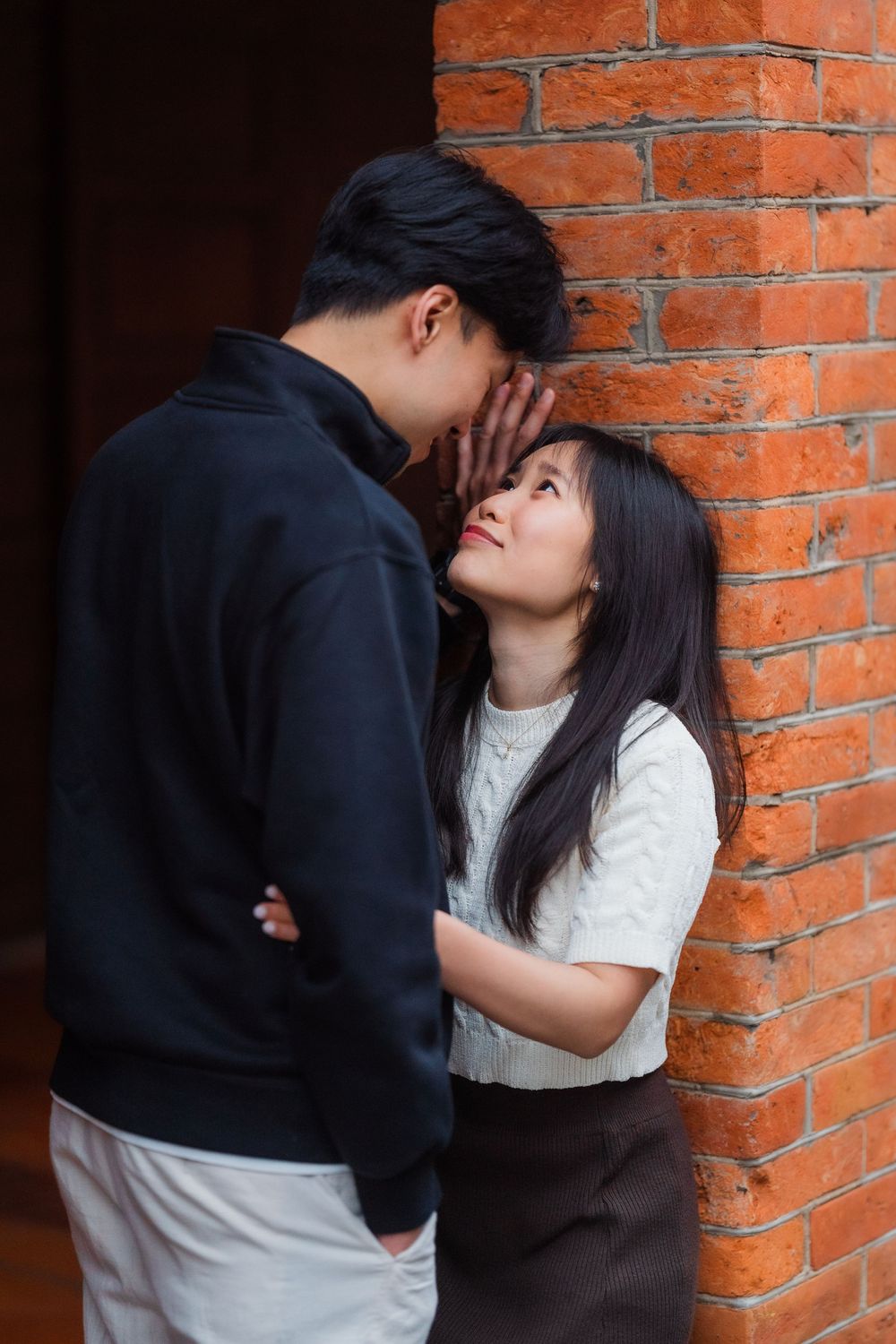 A couple shares an intimate moment against a rustic brick wall backdrop.