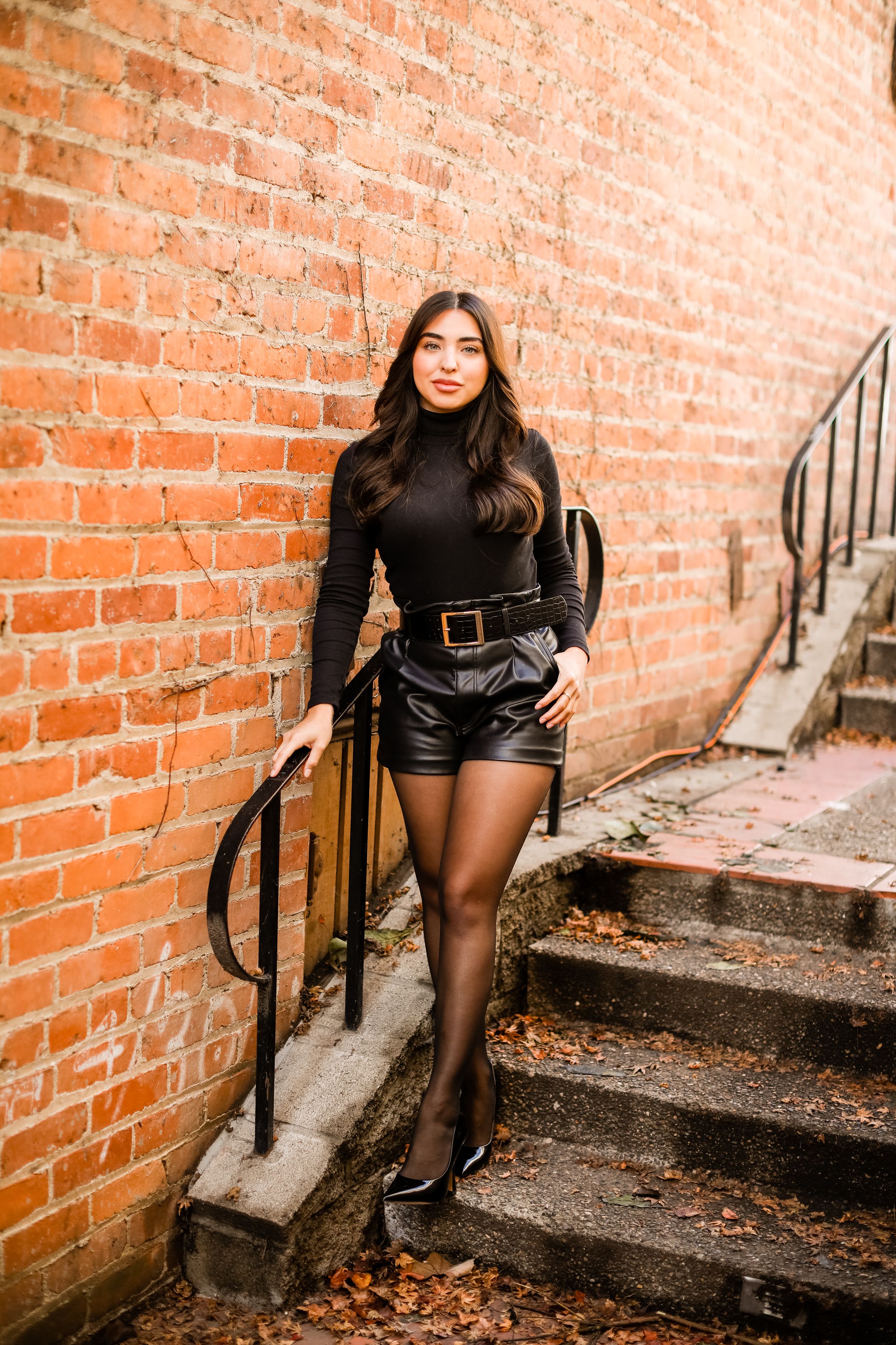 Stylish pose on brick steps wearing black turtleneck and leather shorts with tights.