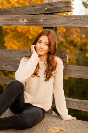 Casual autumn portrait on wooden bench wearing cream sweater and dark jeans.
