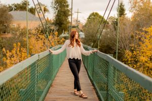 Walking across suspension bridge during golden hour in casual autumn attire.