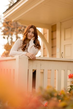 Warm sunset portrait leaning on white porch railing in cream sweater.