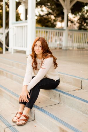 Casual autumn portrait sitting on white steps wearing cream sweater and sandals.