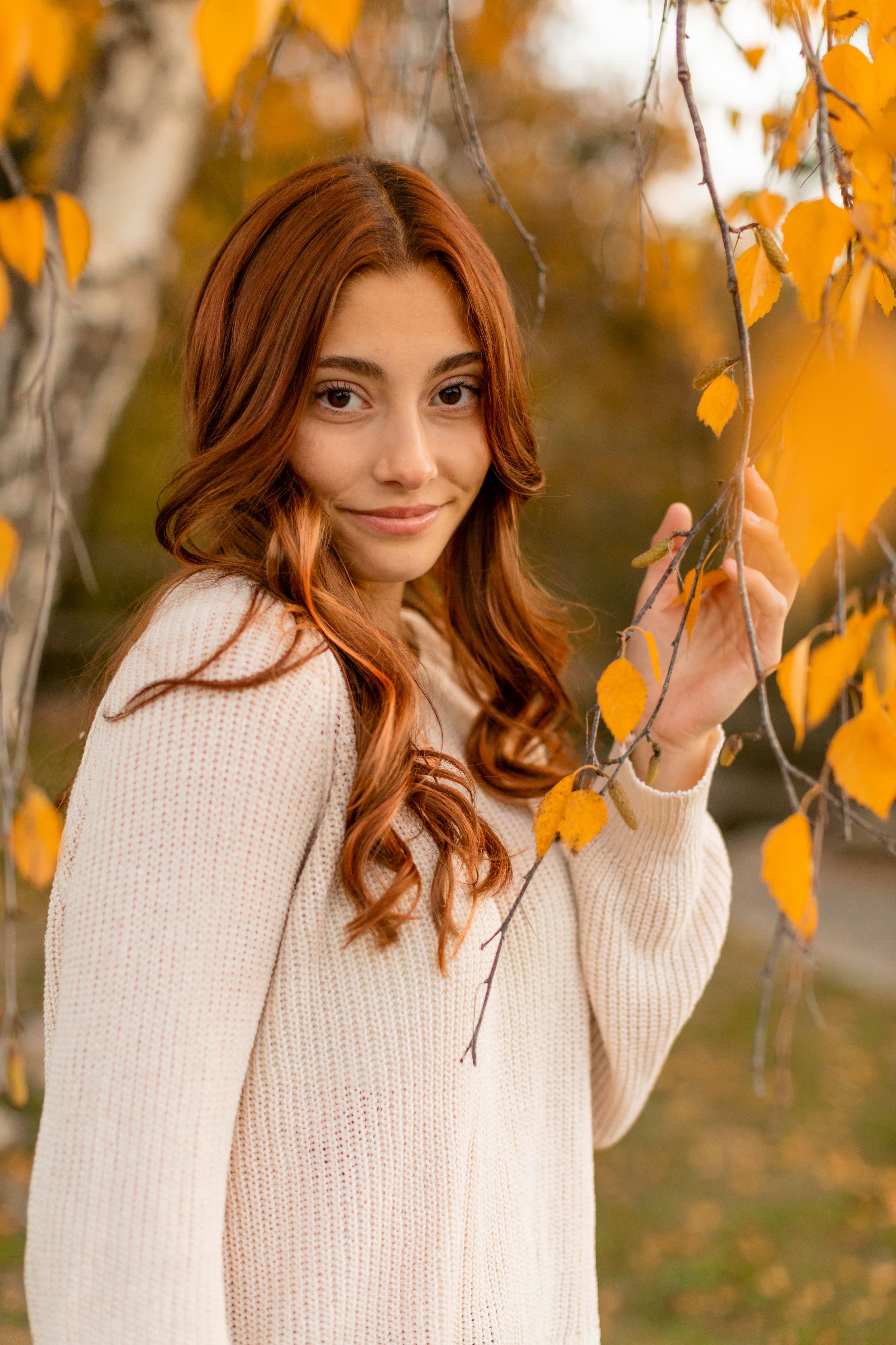 Autumn portrait among yellow leaves wearing cream knit sweater with warm lighting.