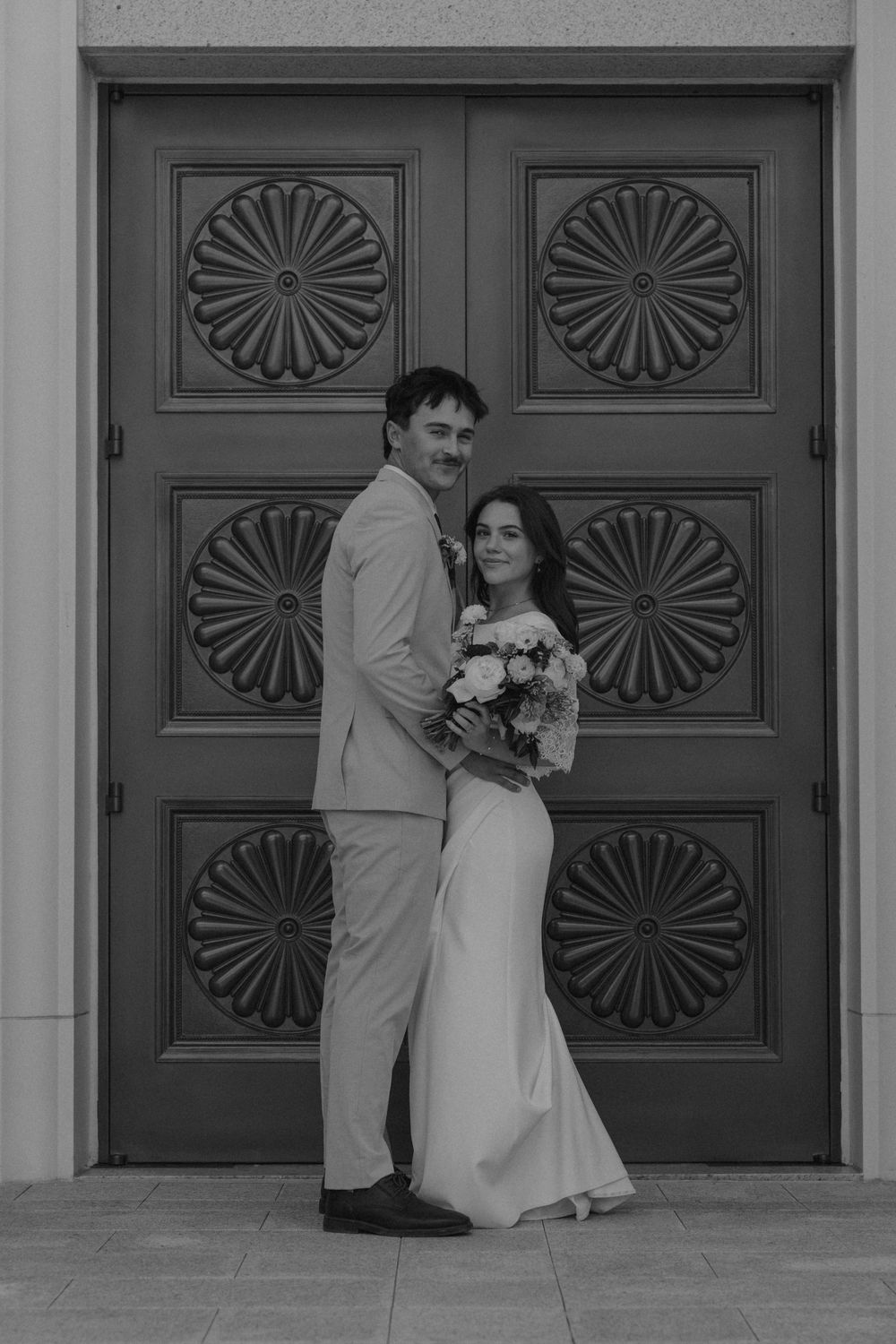 A black and white wedding photo series showing a couple posing in front of ornate wooden doors with fan designs.