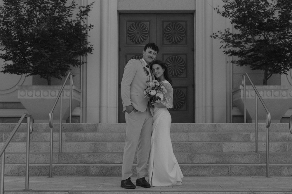A bride and groom share romantic moments in front of a grand building entrance during their wedding photo session.