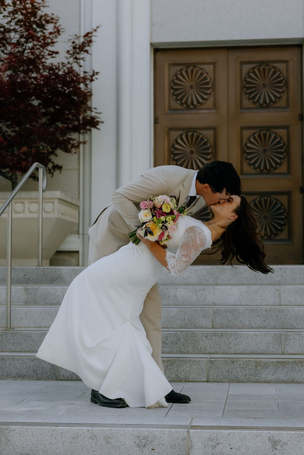 A romantic wedding couple performs a dip pose on marble steps in front of an ornate door.