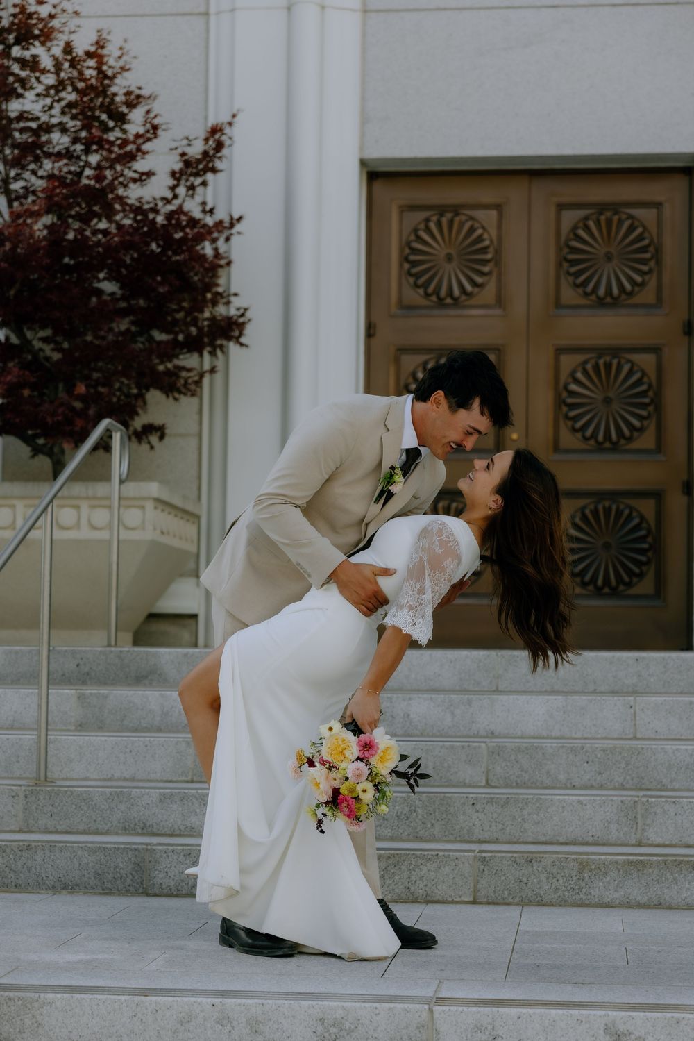 A couple shares a dramatic dip kiss on church steps with the bride holding a colorful bouquet.