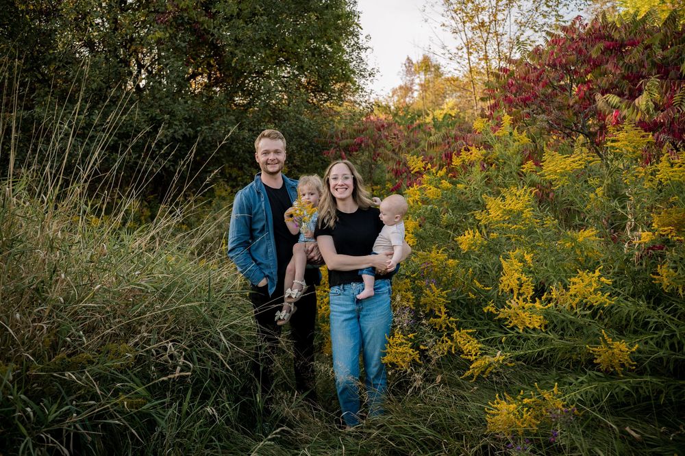 Couple embraces in a lush garden setting with vibrant fall foliage and golden afternoon sunlight.