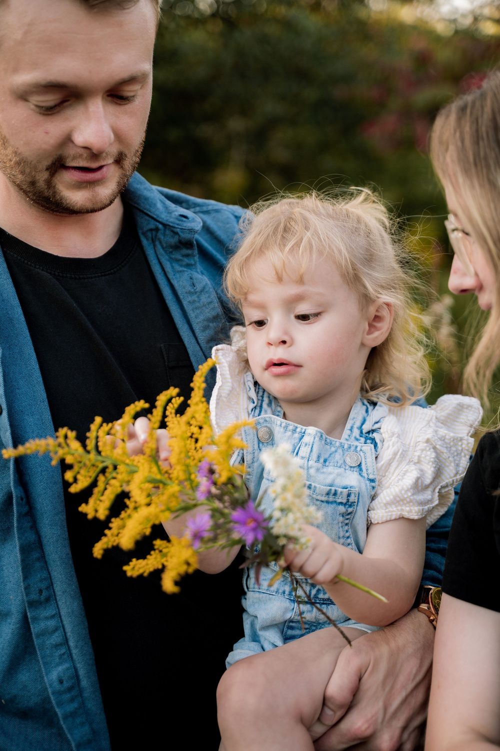 Family shares tender moments among blooming yellow goldenrod flowers in an outdoor nature setting.