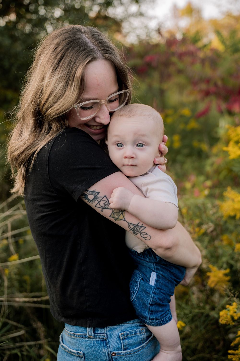 A tender moment between parent and baby against a backdrop of autumn foliage in a garden setting.
