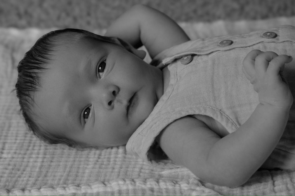 Black and white portrait of infant lying on textured blanket.