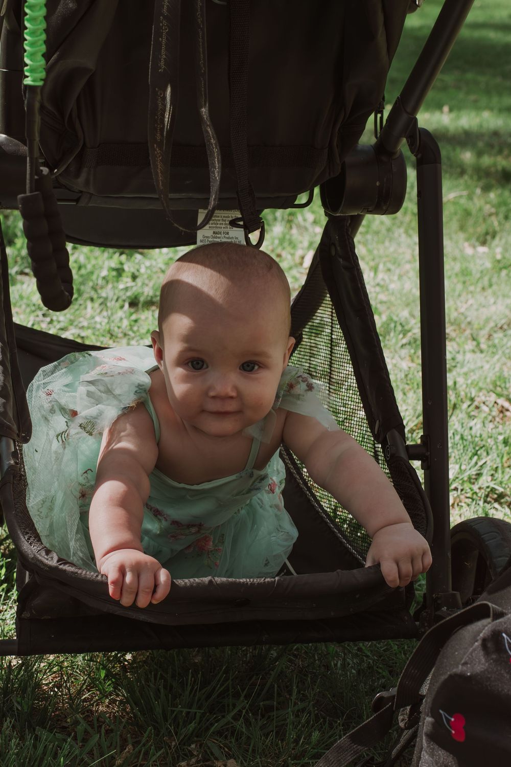 Baby wearing mint green outfit peeks through the bottom of a stroller with a playful expression.